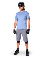 Shorts Alpinestars A-Dura, shorts de MTB, gris oscuro, usados por un ciclista con un jersey azul claro, casco de MTB negro, guantes negros y rodilleras, equipamiento completo de montaña para trail y conducción off-road