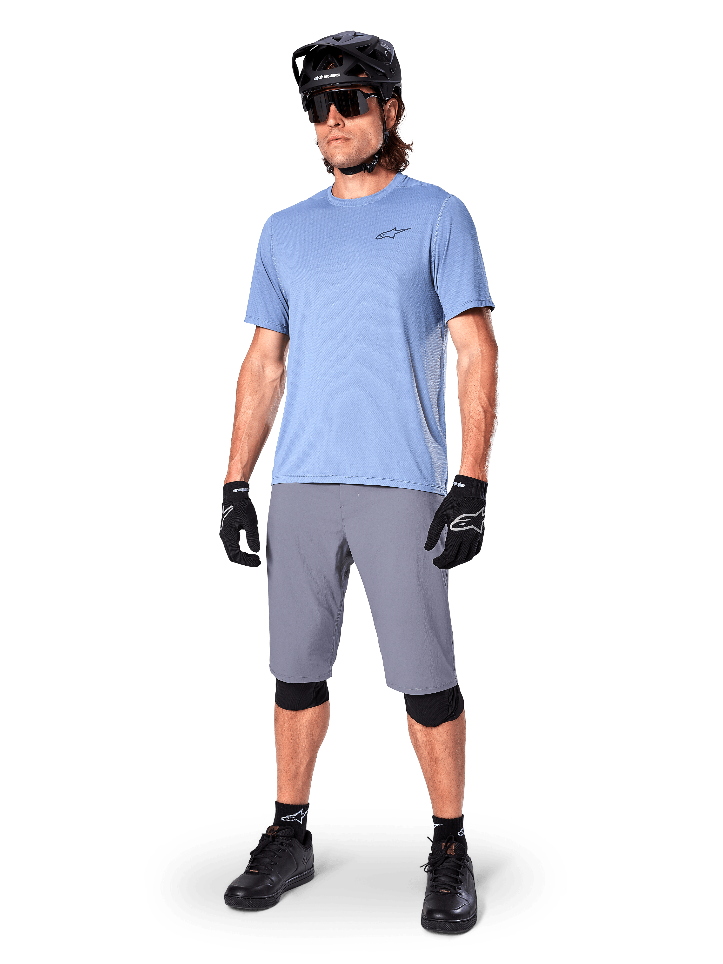 Shorts Alpinestars A-Dura, shorts de MTB, gris oscuro, usados por un ciclista con un jersey azul claro, casco de MTB negro, guantes negros y rodilleras, equipamiento completo de montaña para trail y conducción off-road
