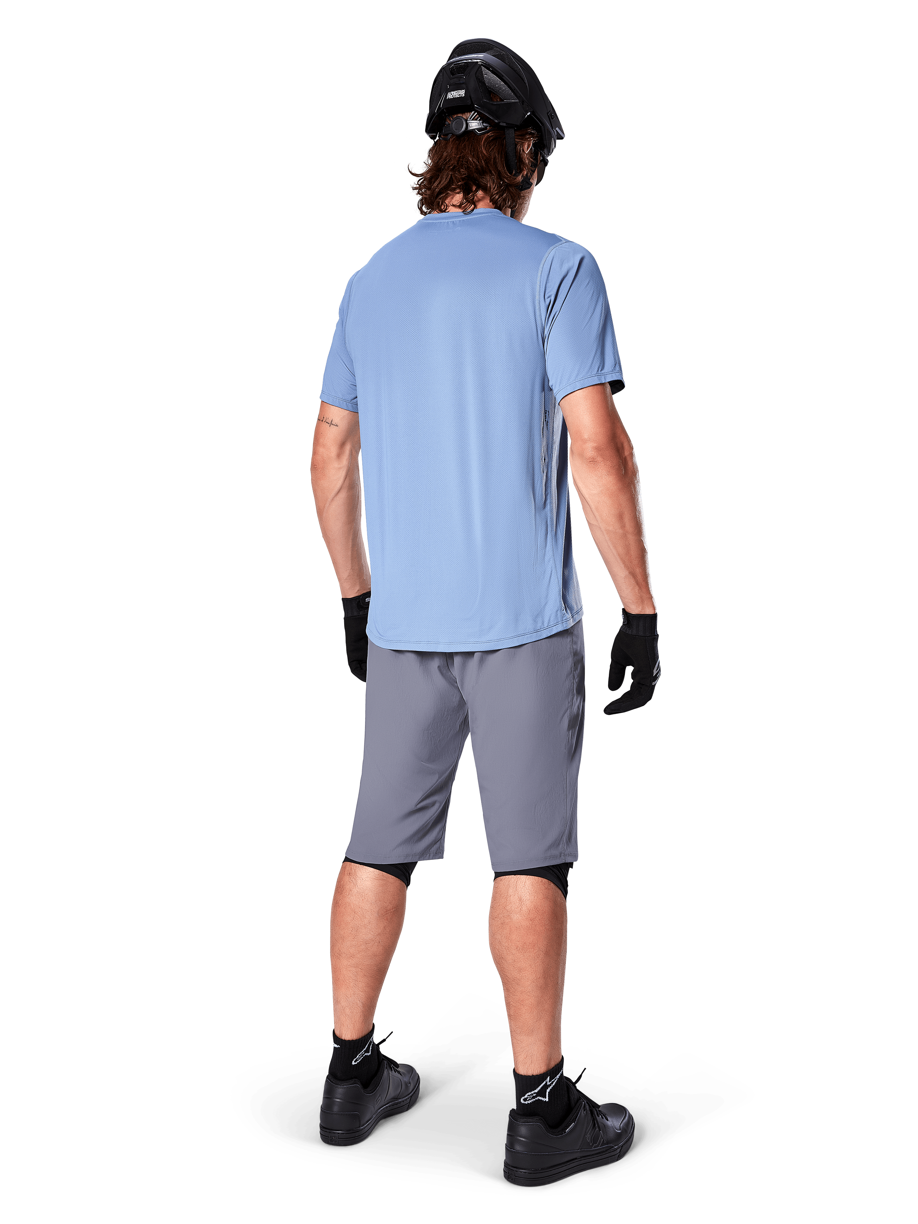Shorts Alpinestars A-Dura, shorts de MTB en gris oscuro, vista trasera, combinados con un jersey de manga corta azul claro, casco de MTB negro, guantes y calcetines negros con calzado negro, equipamiento funcional y duradero para ciclismo de montaña