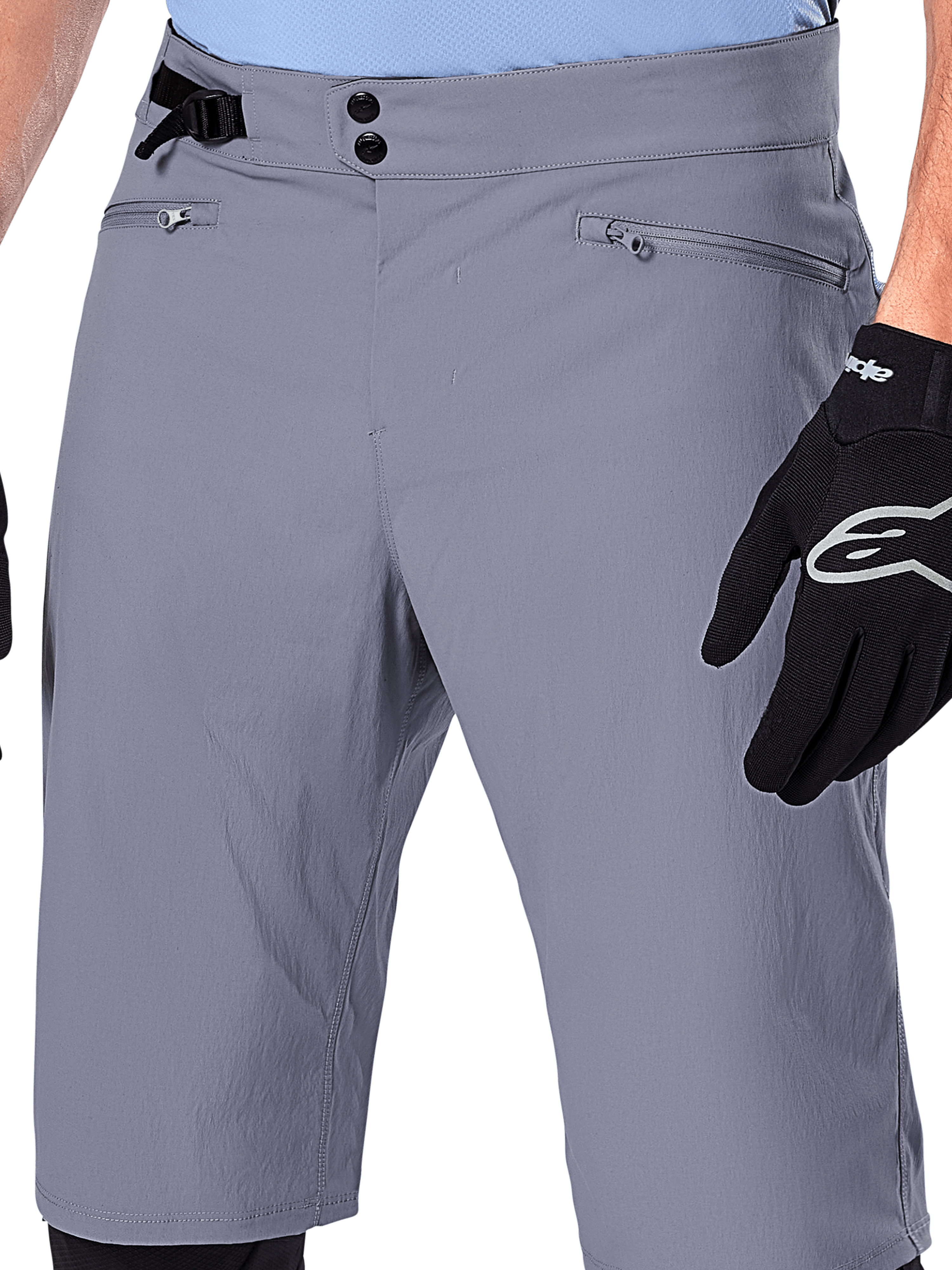 Alpinestars A-Dura Shorts, shorts de MTB, gris oscuro, vista de cerca de la cintura que muestra el cierre de doble broche, ajustador lateral de cintura y bolsillos con cremallera, combinados con guantes de ciclismo negros, ropa duradera para ciclismo de montaña.