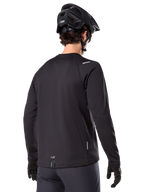 Jersey Térmico Alpinestars A-Dura, jersey de ciclismo de montaña de manga larga, negro, vista trasera que muestra la cola extendida, pequeños detalles reflectantes y logotipo en el dobladillo, usado con un casco y guantes negros para ciclismo en climas fríos