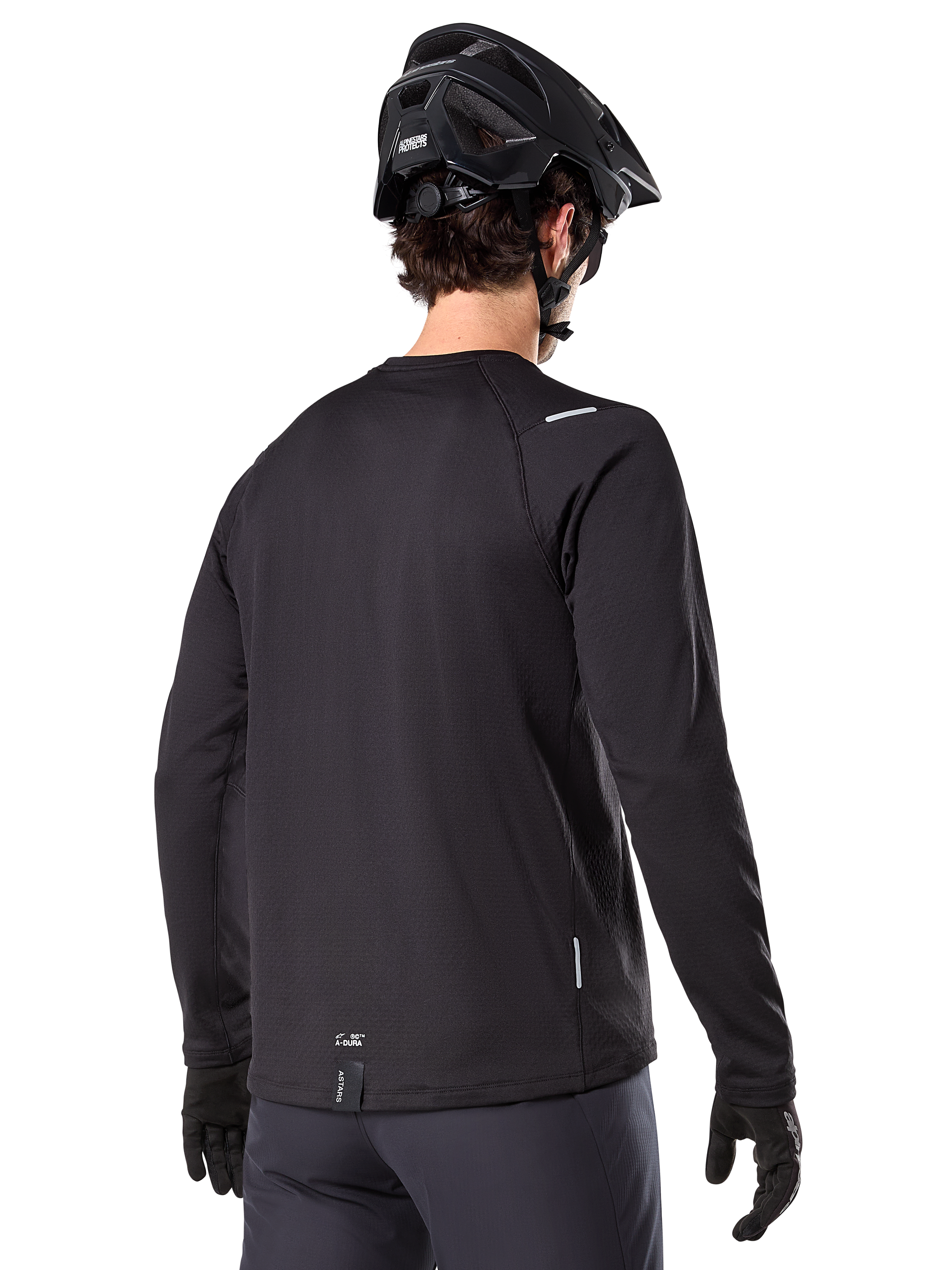 Jersey Térmico Alpinestars A-Dura, jersey de ciclismo de montaña de manga larga, negro, vista trasera que muestra la cola extendida, pequeños detalles reflectantes y logotipo en el dobladillo, usado con un casco y guantes negros para ciclismo en climas fríos