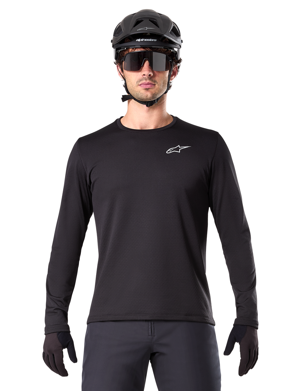 Jersey Térmico Alpinestars A-Dura, jersey de ciclismo de montaña de manga larga en color negro, usado con casco negro y gafas de sol grandes, con un pequeño logotipo blanco de Alpinestars en el pecho, ajuste regular, ropa de ciclismo MTB