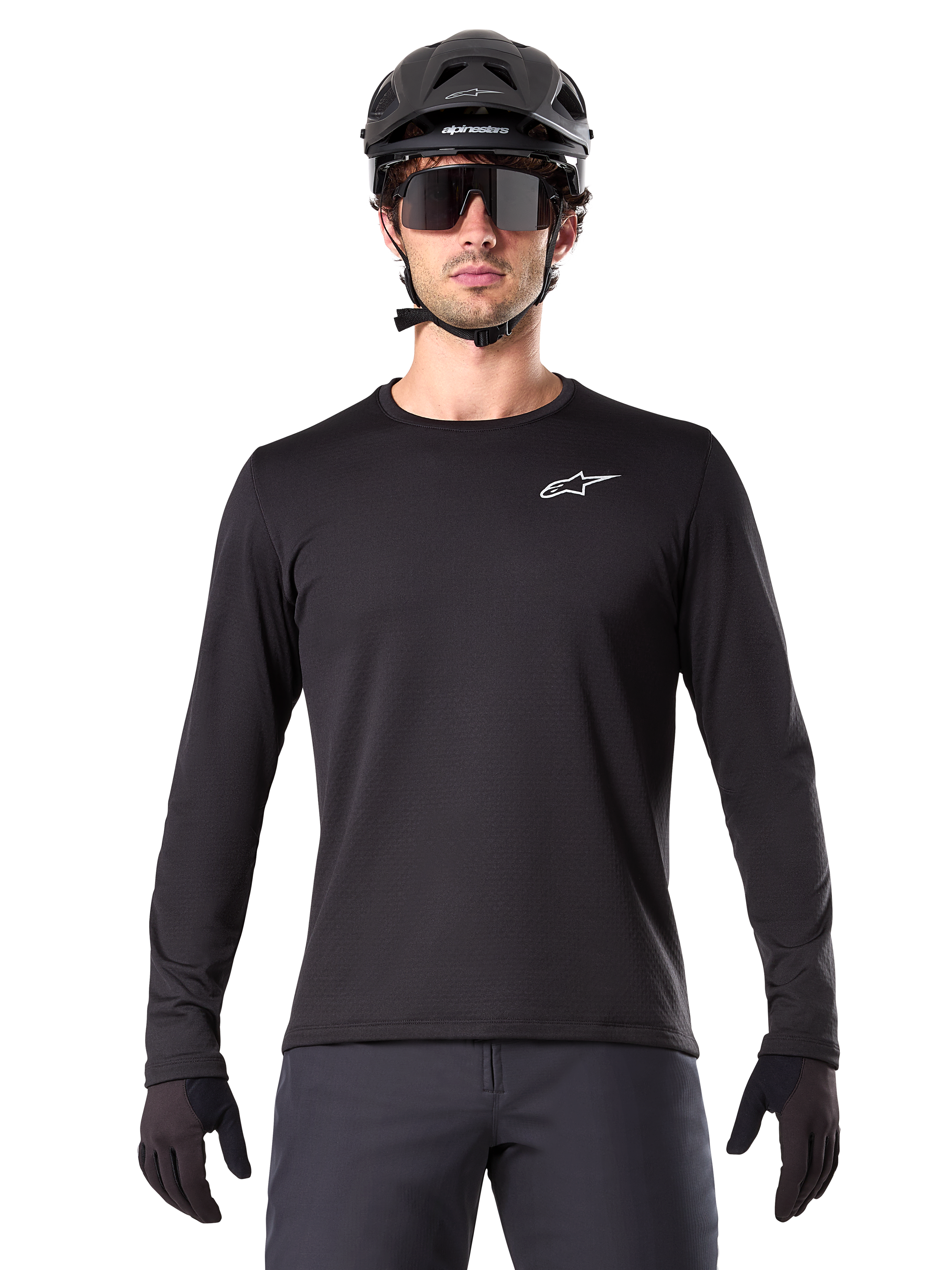 Jersey Térmico Alpinestars A-Dura, jersey de ciclismo de montaña de manga larga en color negro, usado con casco negro y gafas de sol grandes, con un pequeño logotipo blanco de Alpinestars en el pecho, ajuste regular, ropa de ciclismo MTB