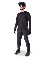 Modelo con el Jersey Térmico Alpinestars A-Dura, jersey de MTB de manga larga negro, casco de MTB negro, gafas de sol y pantalones gris oscuro, con un pequeño logotipo blanco en el pecho y forro polar aislante para montar en climas fríos.