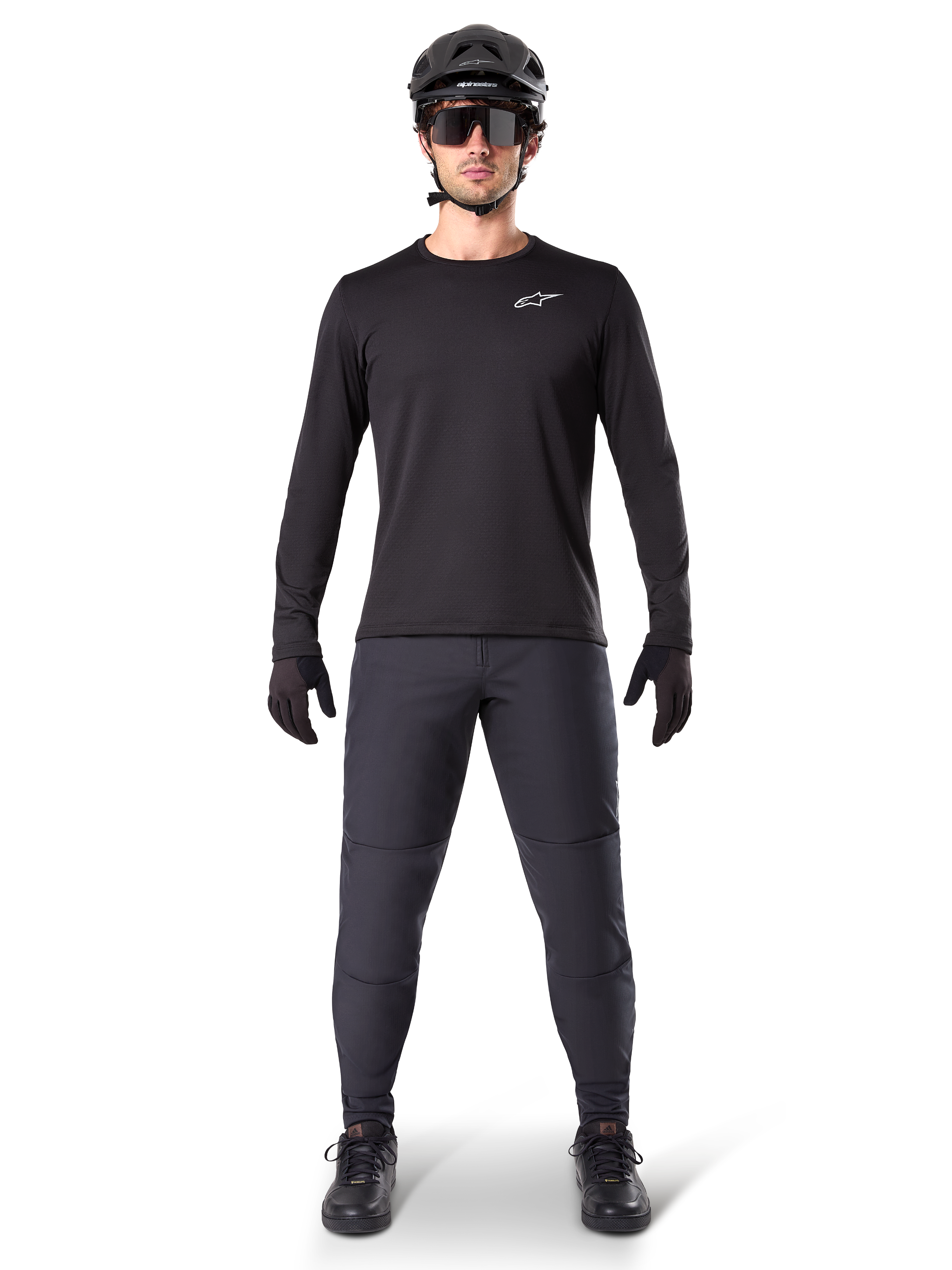 Alpinestars A-Dura Thermal Jersey, jersey de ciclismo de montaña de manga larga, negro, combinado con pantalones gris oscuro, guantes negros, casco negro y gafas de sol, con el logotipo blanco de Alpinestars en el pecho, conjunto coordinado para ciclismo de montaña en climas fríos