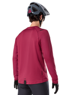 Alpinestars A-Dura Thermal Jersey, jersey de ciclismo de montaña de manga larga, granate, vista trasera en modelo con casco de MTB gris y guantes negros, con cola extendida y pequeños detalles de logotipo, diseñado para ciclismo de montaña en climas fríos