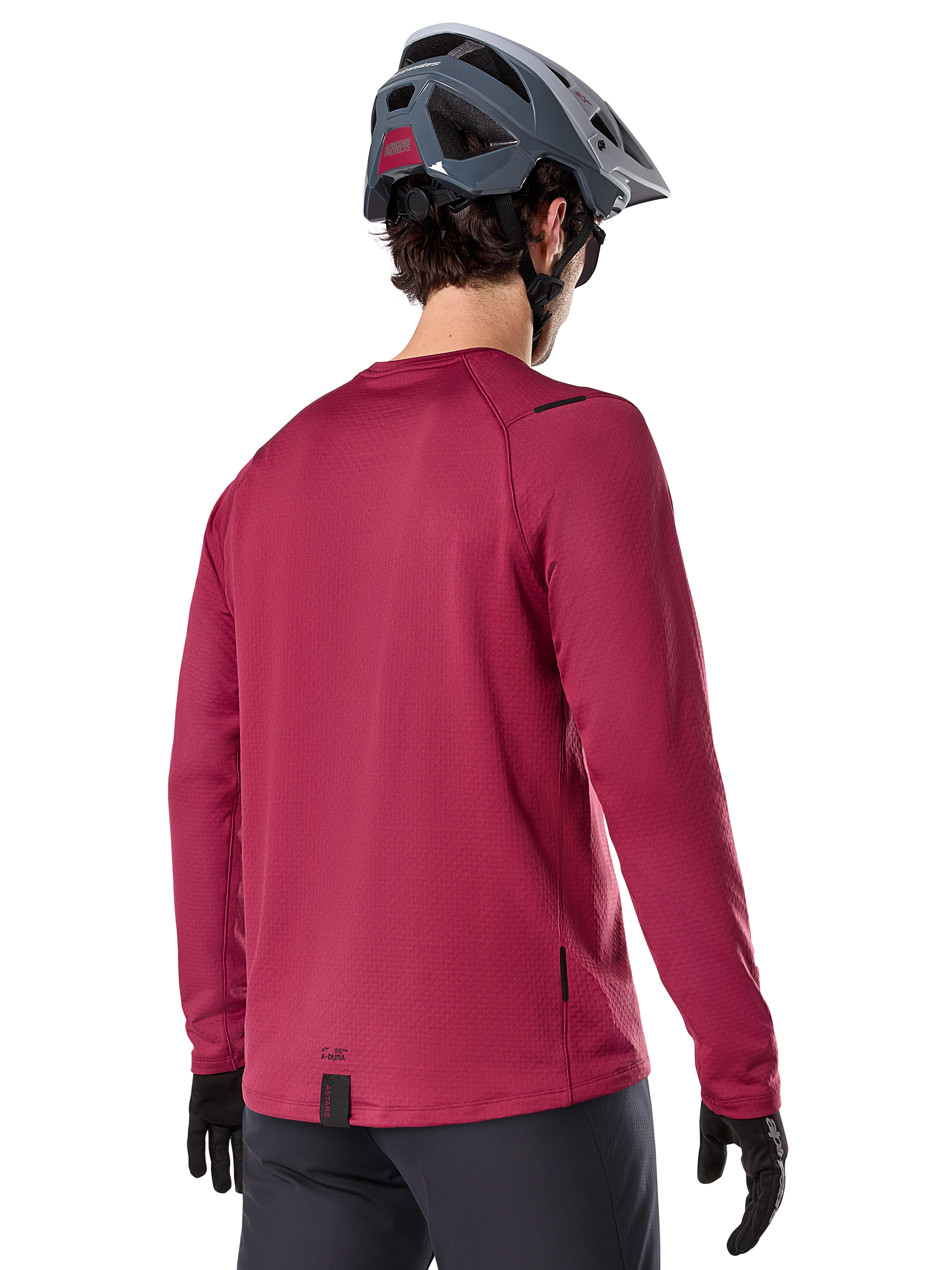 Alpinestars A-Dura Thermal Jersey, jersey de ciclismo de montaña de manga larga, granate, vista trasera en modelo con casco de MTB gris y guantes negros, con cola extendida y pequeños detalles de logotipo, diseñado para ciclismo de montaña en climas fríos