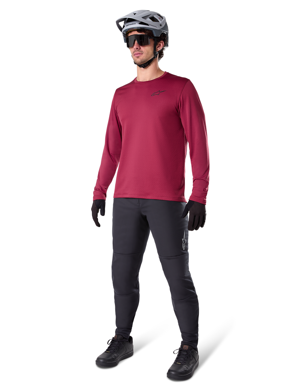 Jersey térmico Alpinestars A-Dura en color granate, camiseta de ciclismo aislante de manga larga combinada con pantalones de ciclismo de montaña gris oscuro, guantes negros y casco gris, toma de estudio de cuerpo completo de equipamiento de MTB para clima frío.