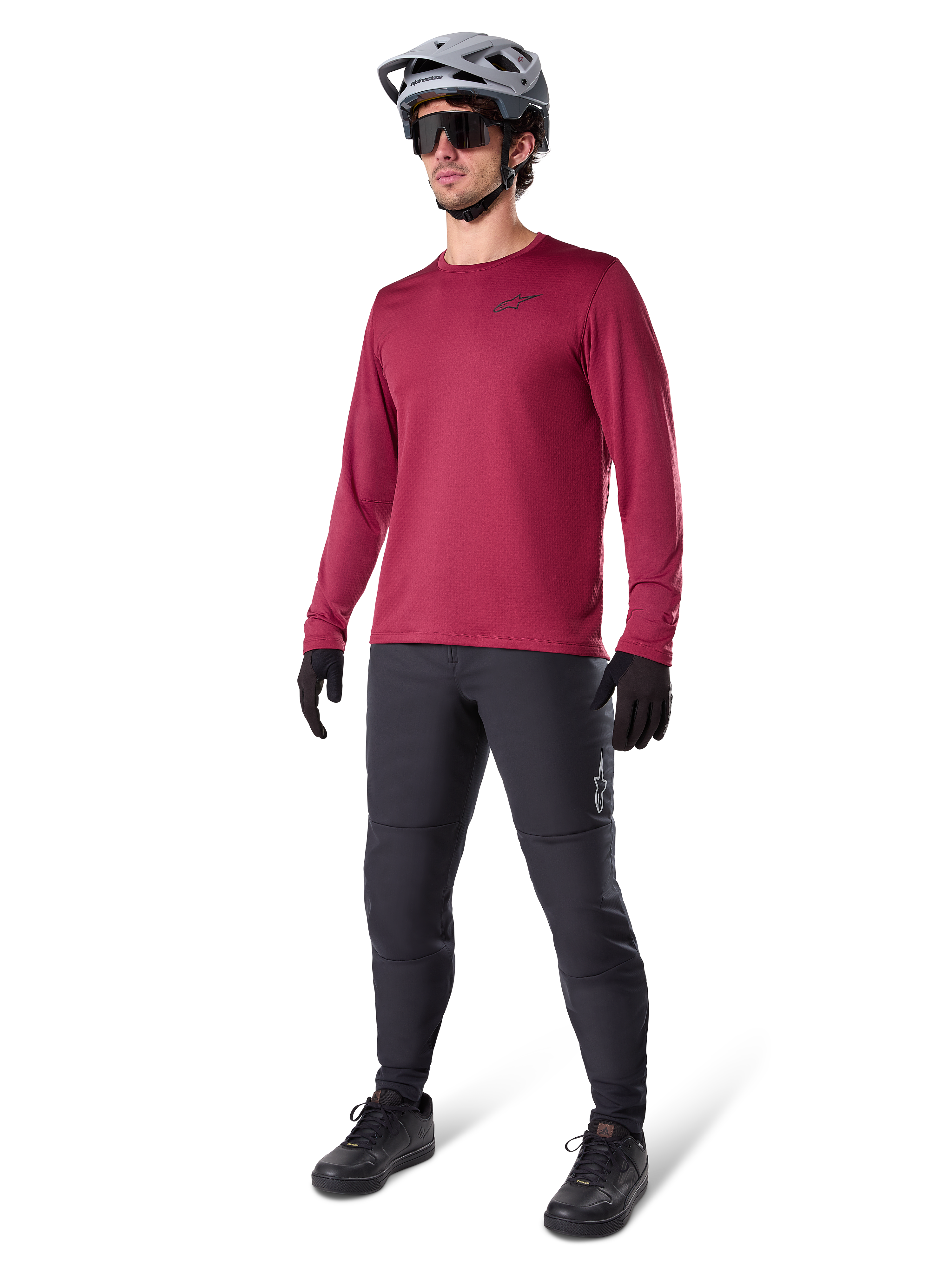 Jersey térmico Alpinestars A-Dura en color granate, camiseta de ciclismo aislante de manga larga combinada con pantalones de ciclismo de montaña gris oscuro, guantes negros y casco gris, toma de estudio de cuerpo completo de equipamiento de MTB para clima frío.
