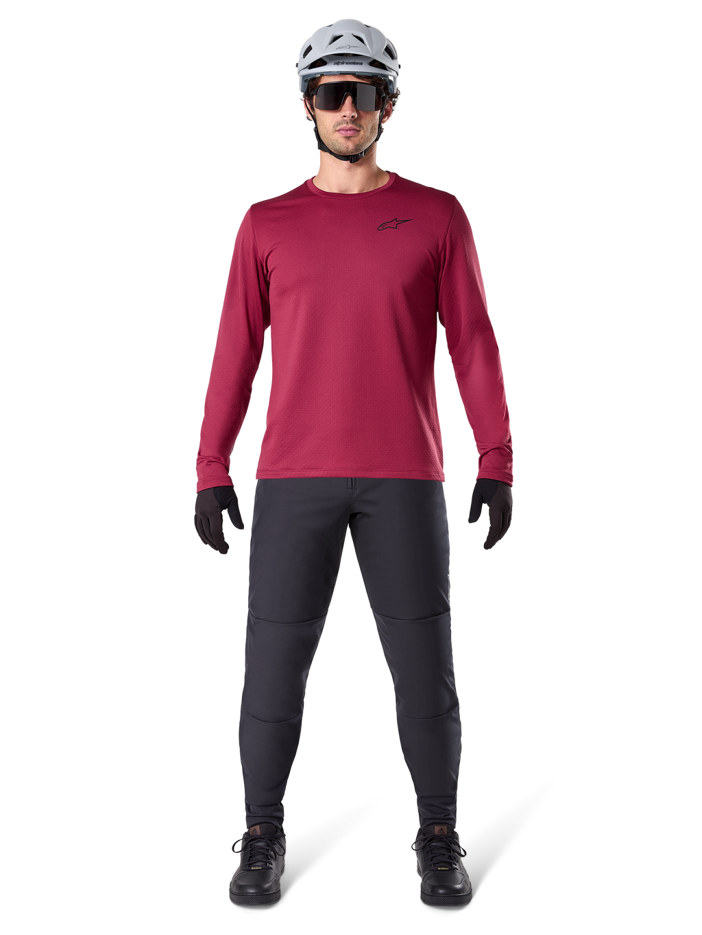 Modelo masculino vistiendo el Jersey Térmico Alpinestars A-Dura en color borgoña, camiseta técnica de ciclismo de manga larga con aislamiento, combinada con pantalones de MTB gris oscuro, casco blanco, gafas de sol negras y guantes negros, equipamiento profesional de MTB para clima frío