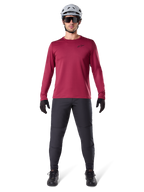 Modelo masculino vistiendo el Jersey Térmico Alpinestars A-Dura en color borgoña, camiseta técnica de ciclismo de manga larga con aislamiento, combinada con pantalones de MTB gris oscuro, casco blanco, gafas de sol negras y guantes negros, equipamiento profesional de MTB para clima frío