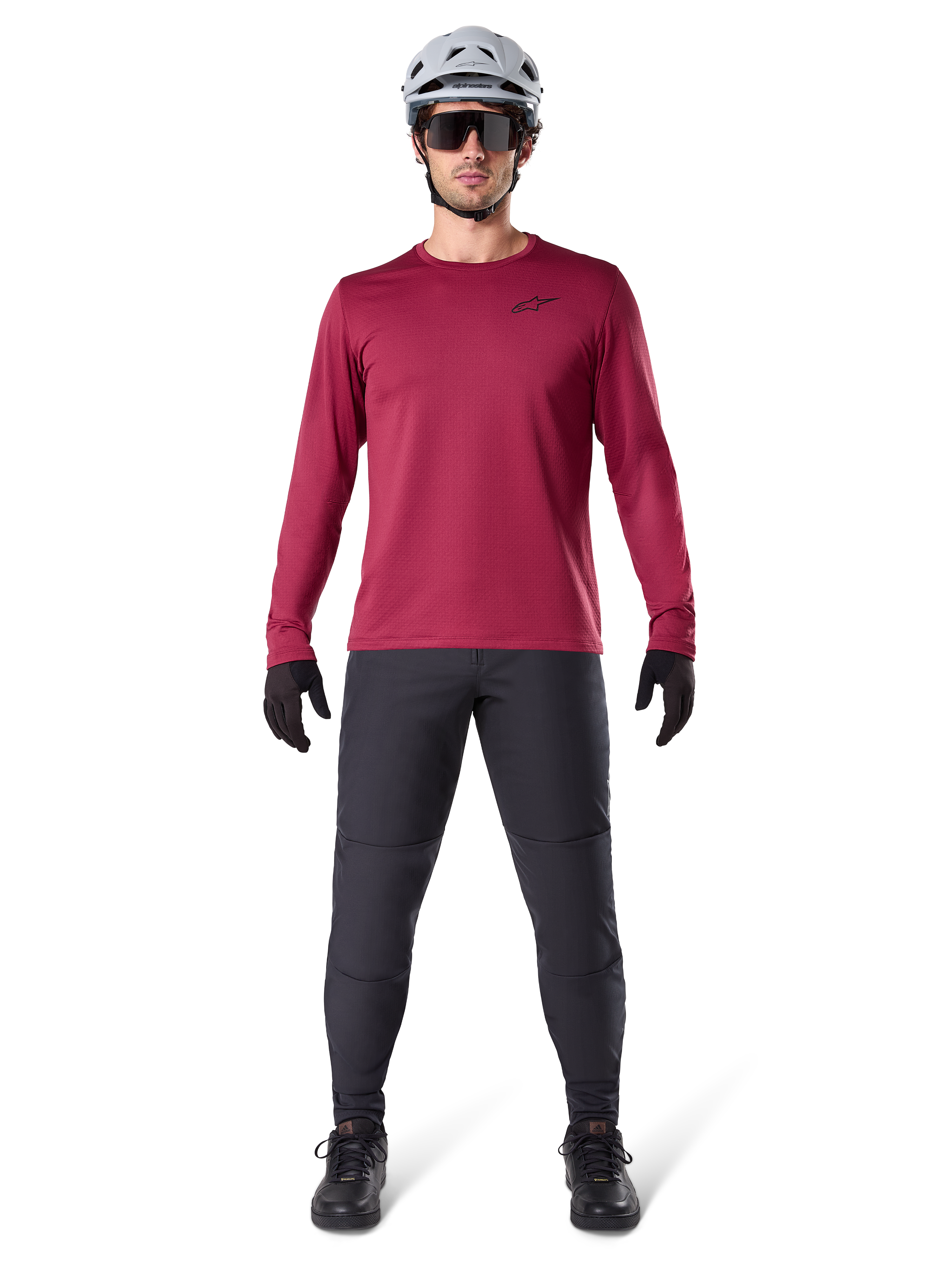 Modelo masculino vistiendo el Jersey Térmico Alpinestars A-Dura en color borgoña, camiseta técnica de ciclismo de manga larga con aislamiento, combinada con pantalones de MTB gris oscuro, casco blanco, gafas de sol negras y guantes negros, equipamiento profesional de MTB para clima frío