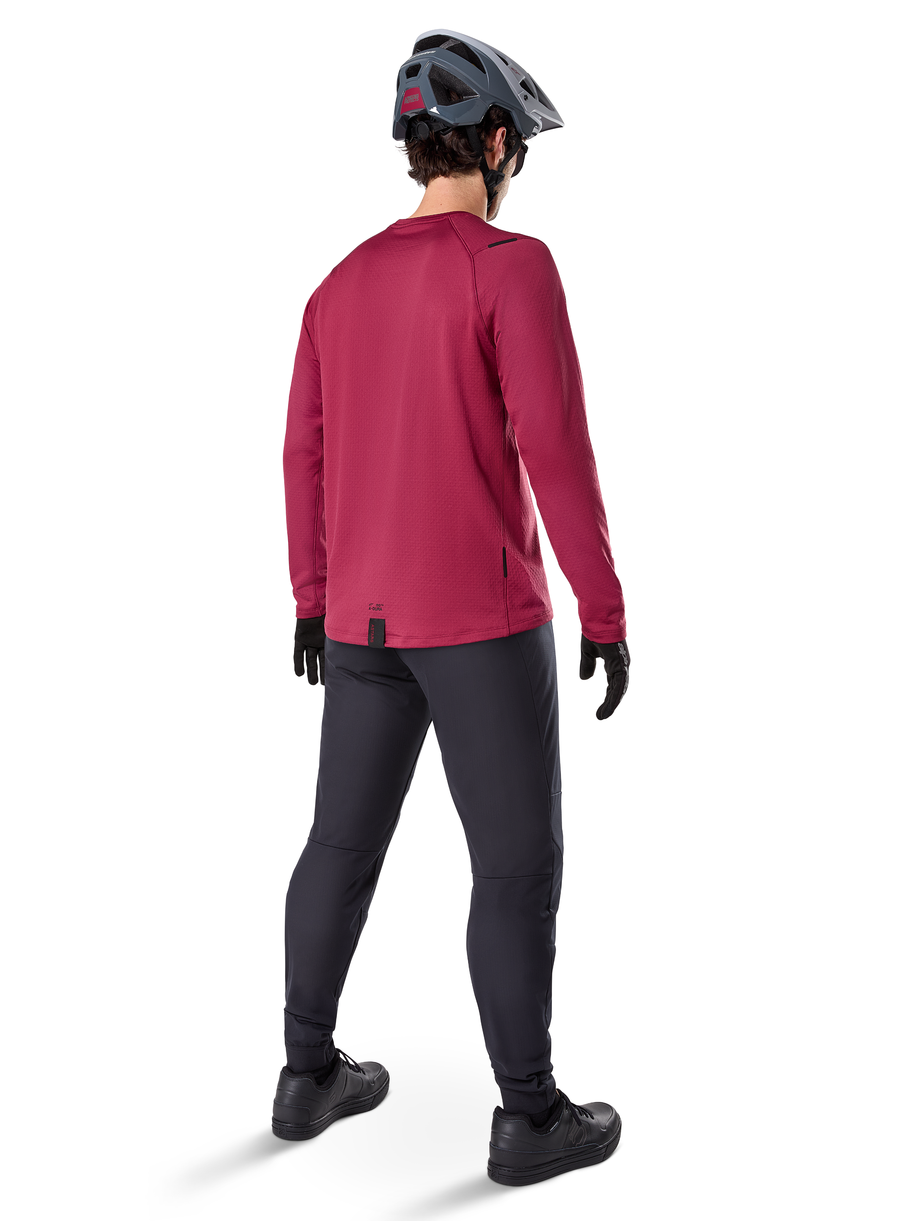 Alpinestars A-Dura Thermal Jersey, jersey de ciclismo de manga larga en color burdeos, vista trasera, combinado con pantalones negros de bicicleta de montaña y casco gris, con dobladillo trasero extendido para mayor cobertura, equipamiento de MTB para clima frío