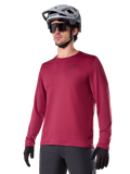 Alpinestars A-Dura Thermal Jersey, jersey de manga larga para ciclismo de montaña, rojo borgoña, con forro polar aislante y un pequeño logotipo negro en el pecho, usado con un casco gris, gafas de sol negras y guantes negros, diseñado para ciclismo en climas fríos