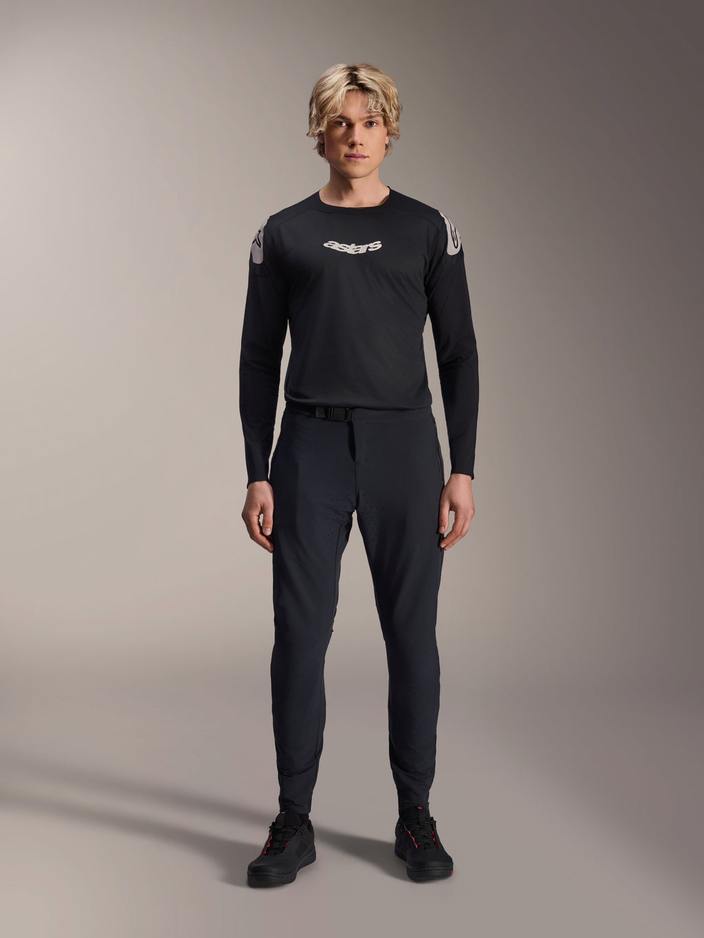 Alpinestars A-Aria Elite Pants, pantalones de MTB Black Titanium, usados por un modelo masculino con un jersey de manga larga negro a juego y zapatillas, diseño de rendimiento con ajuste slim y cierre de hebilla magnética, ropa técnica para bicicleta de montaña