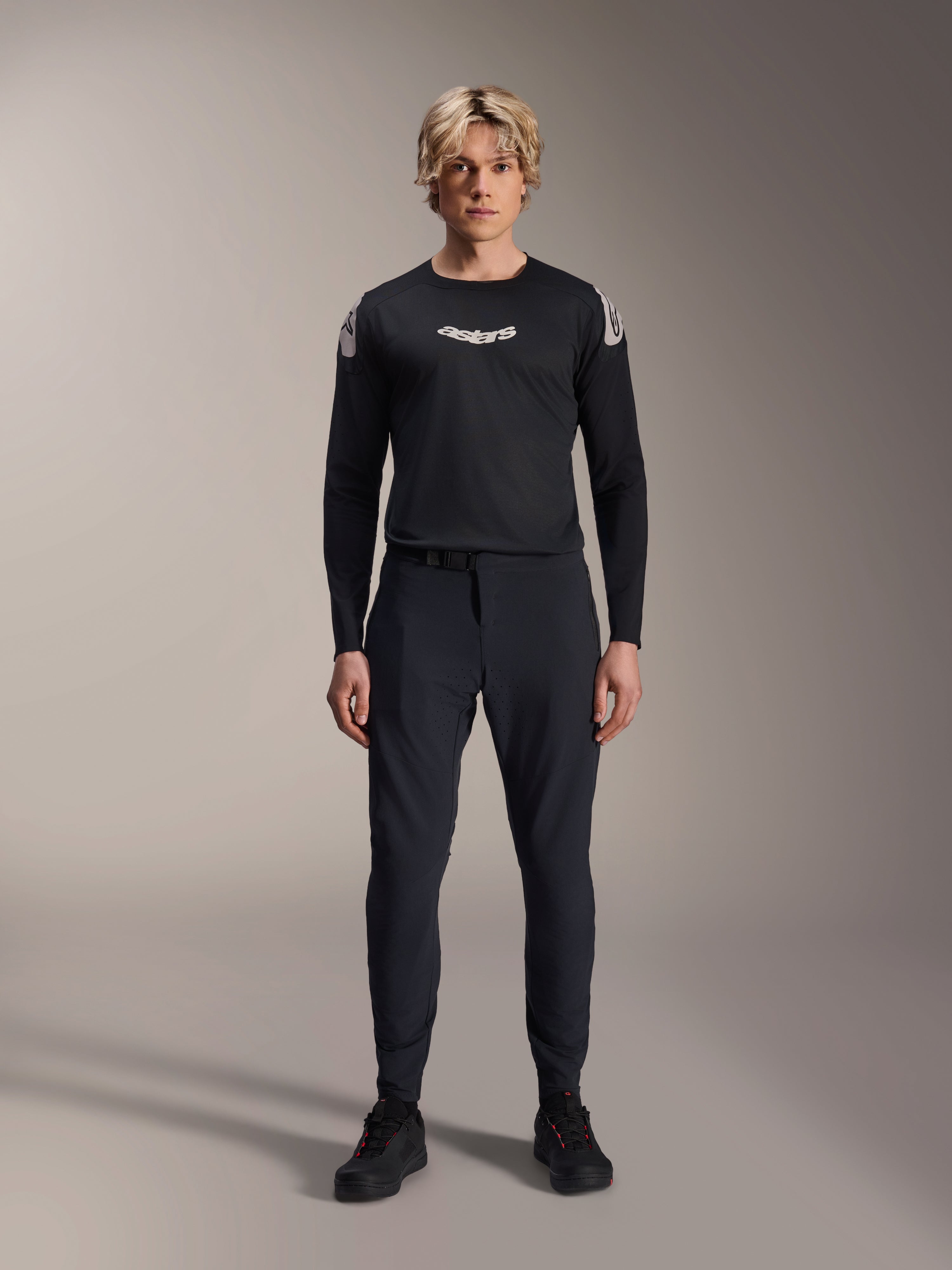 Alpinestars A-Aria Elite Pants, pantalones de MTB Black Titanium, usados por un modelo masculino con un jersey de manga larga negro a juego y zapatillas, diseño de rendimiento con ajuste slim y cierre de hebilla magnética, ropa técnica para bicicleta de montaña