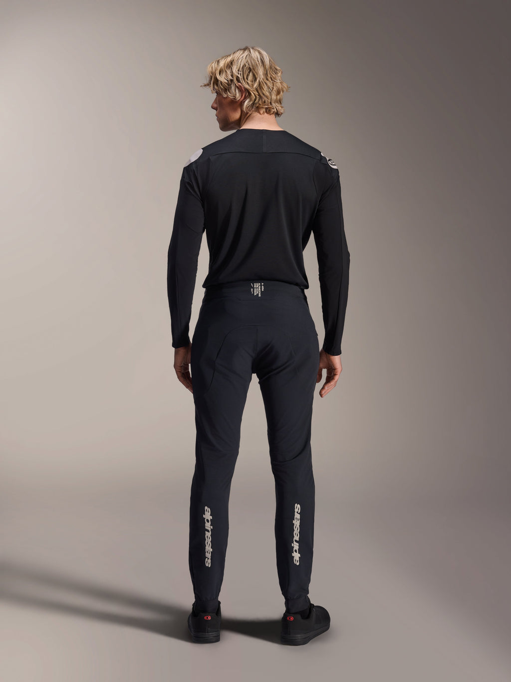 Jersey de manga larga Alpinestars A-Aria Polartec Elite, jersey de MTB negro, vista trasera usado con pantalones negros a juego, ajuste de rendimiento para ciclismo de montaña, con tejido técnico que absorbe la humedad y marca sutil en la parte inferior de la espalda