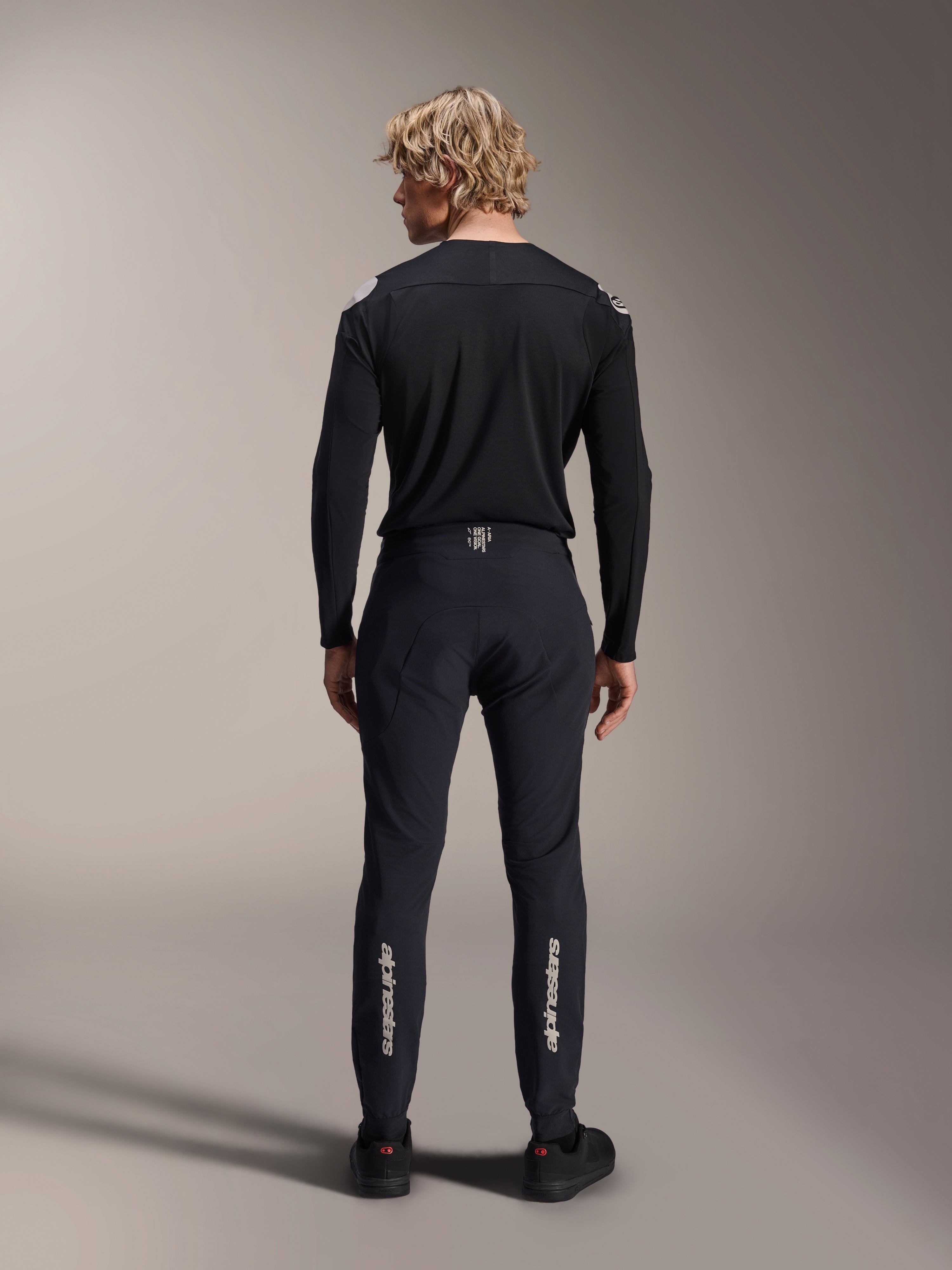 Pantalones Alpinestars A-Aria Elite, Black Titanium, vista trasera en modelo masculino, con la marca Alpinestars en plateado en la parte inferior de las piernas, pantalones técnicos de MTB con ajuste de alto rendimiento y detalle de cintura que absorbe la humedad.