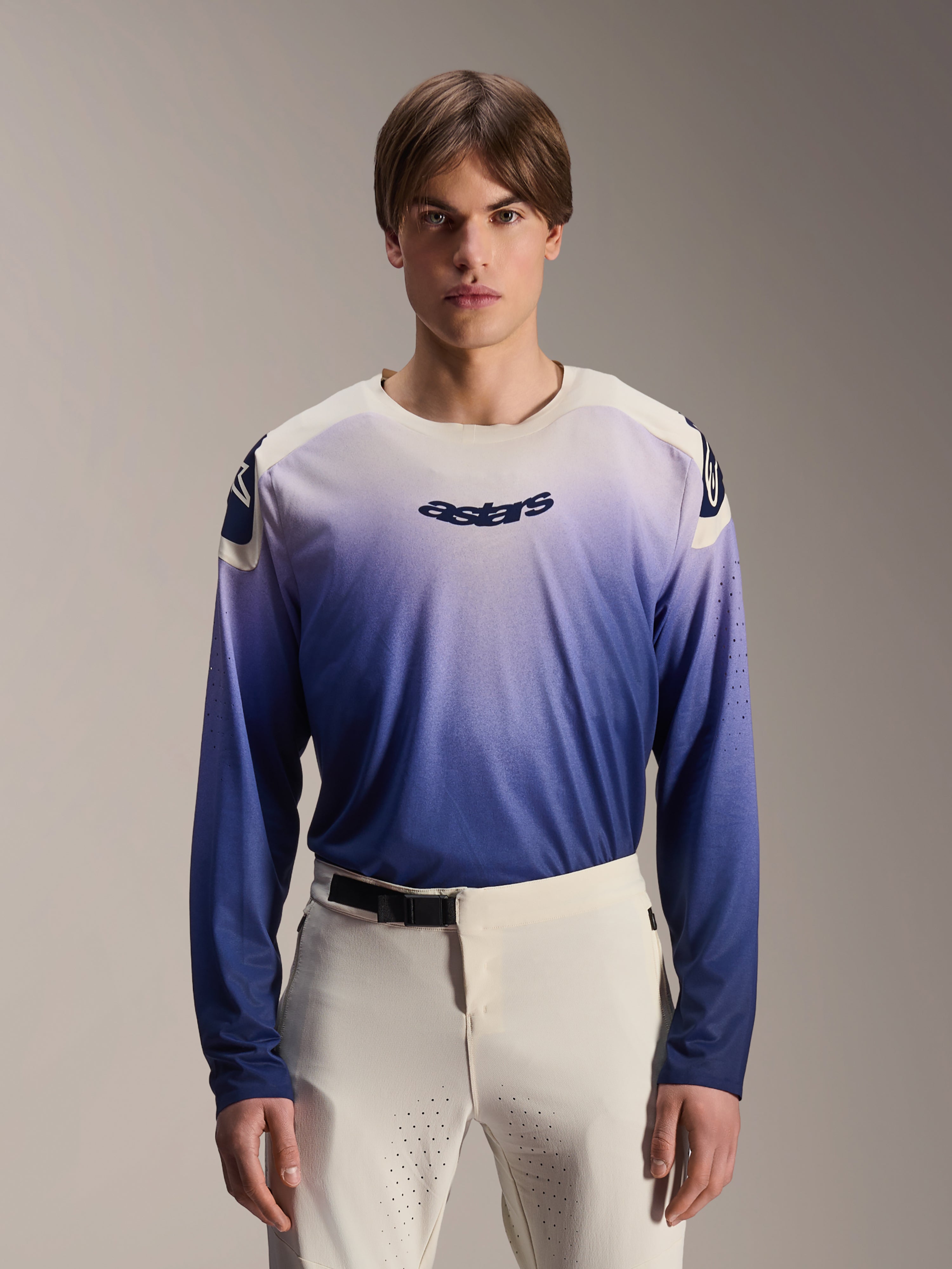 Alpinestars A-Aria Polartec Maker Elite Jersey, jersey de MTB de manga larga, color Baja Blue con degradado de blanco a azul, usado por un modelo con pantalones blancos, con logotipo azul oscuro en el pecho y perforaciones láser en las mangas, ropa de ciclismo de montaña de alto rendimiento