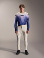 Alpinestars A-Aria Elite Pants, pantalones de MTB de alto rendimiento en color crudo, pantalones de ciclismo blanco roto con paneles perforados con láser en los muslos y hebilla magnética, combinados con camiseta de manga larga con degradado azul y zapatillas negras, ajuste de rendimiento para trail