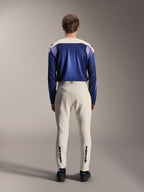 Alpinestars A-Aria Polartec Maker Elite Long Sleeve Jersey, azul Baja y blanco roto, vista trasera de un modelo con equipamiento técnico de bicicleta de montaña, incluyendo pantalones blanco roto con la marca Alpinestars en la parte inferior de las piernas, conjunto de ciclismo de alto rendimiento para senderos