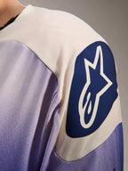 Alpinestars A-Aria Polartec Maker Elite Jersey, jersey de manga larga para ciclismo de montaña, azul Baja y blanco, primer plano del hombro con un gran logotipo circular azul de Alpinestars con una estrella blanca, mostrando las perforaciones láser y la textura del tejido técnico