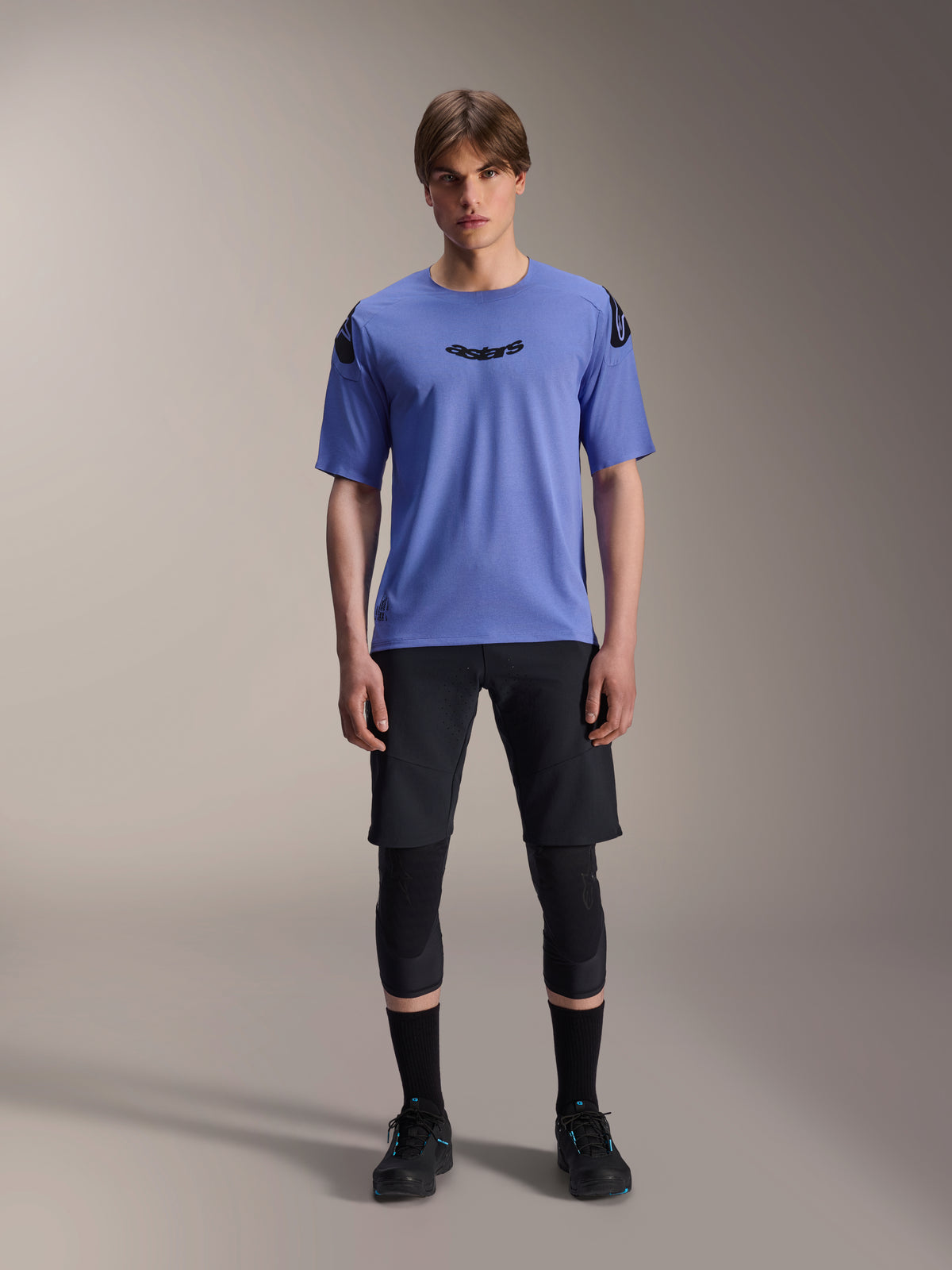 Alpinestars A-Aria Lite Short, pantalones cortos de ciclismo de montaña para hombre, negros, usados con jersey de manga corta morado claro y rodilleras negras, ropa técnica de MTB para alto rendimiento
