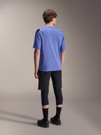 Jersey de manga corta Alpinestars A-Aria Polartec Elite en color Baja Blue, vista trasera en un modelo masculino, combinado con pantalones cortos de MTB negros y rodilleras, con un ajuste de rendimiento y dobladillo trasero más largo para trail.