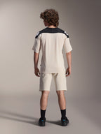 Alpinestars A-Aria Elite Shorts y Jersey A-Aria Polartec Elite de manga corta, color crudo con paneles negros en los hombros, vista trasera de un modelo con equipamiento de alto rendimiento para bicicleta de montaña, combinado con calcetines y zapatillas negros