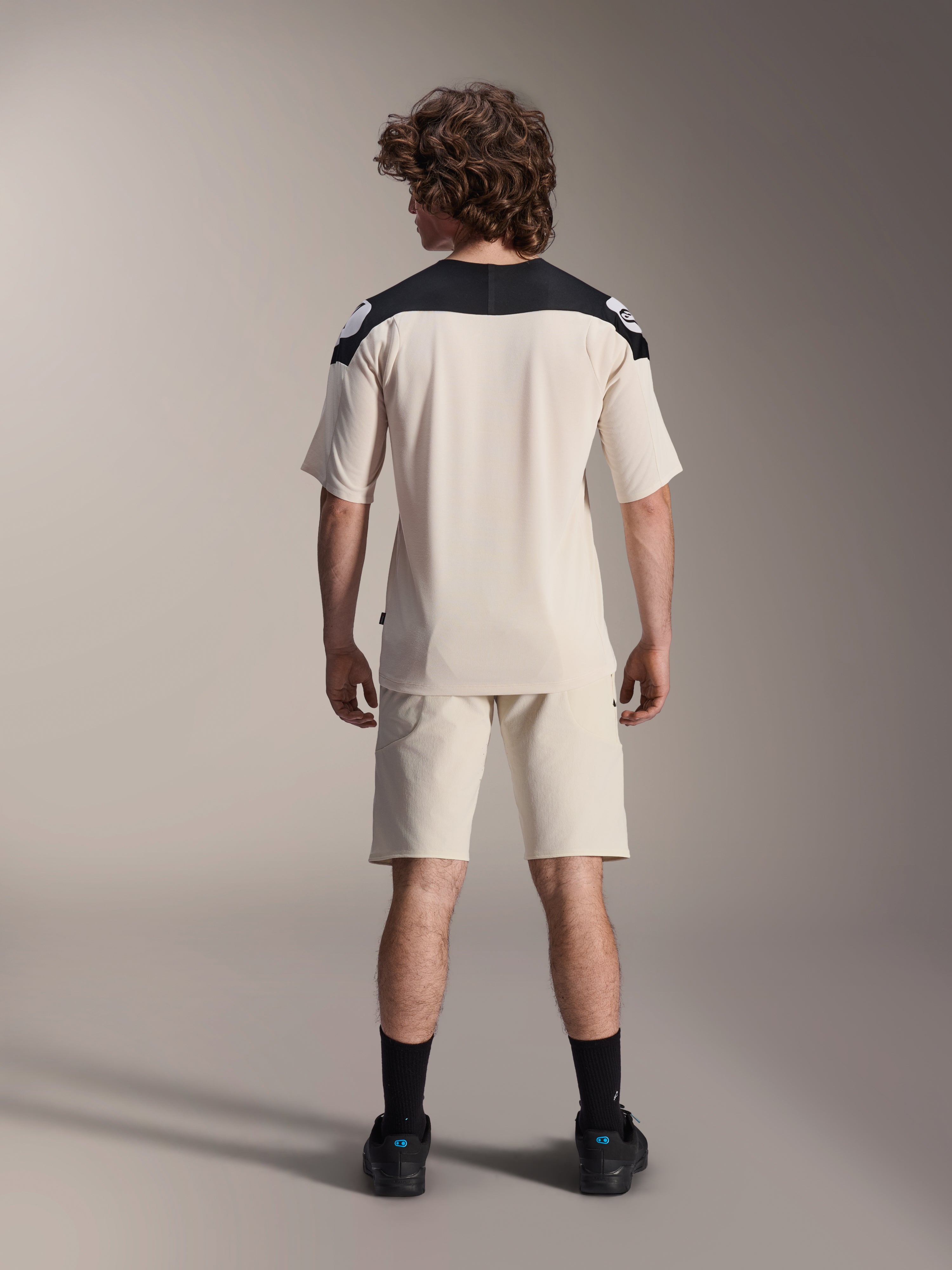 Jersey de manga corta Alpinestars A-Aria Polartec Elite, jersey de ciclismo MTB, color crudo con paneles negros en los hombros, vista trasera mostrada con pantalones cortos a juego y calcetines negros, ajuste de rendimiento con un diseño de cola caída para conducción fuera de carretera.