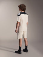 Modelo luciendo el jersey de manga corta Alpinestars A-Aria Polartec Elite en color crudo, visto desde atrás, con paneles negros en los hombros y logotipo blanco, combinado con pantalones cortos de ciclismo de montaña a juego y zapatillas negras