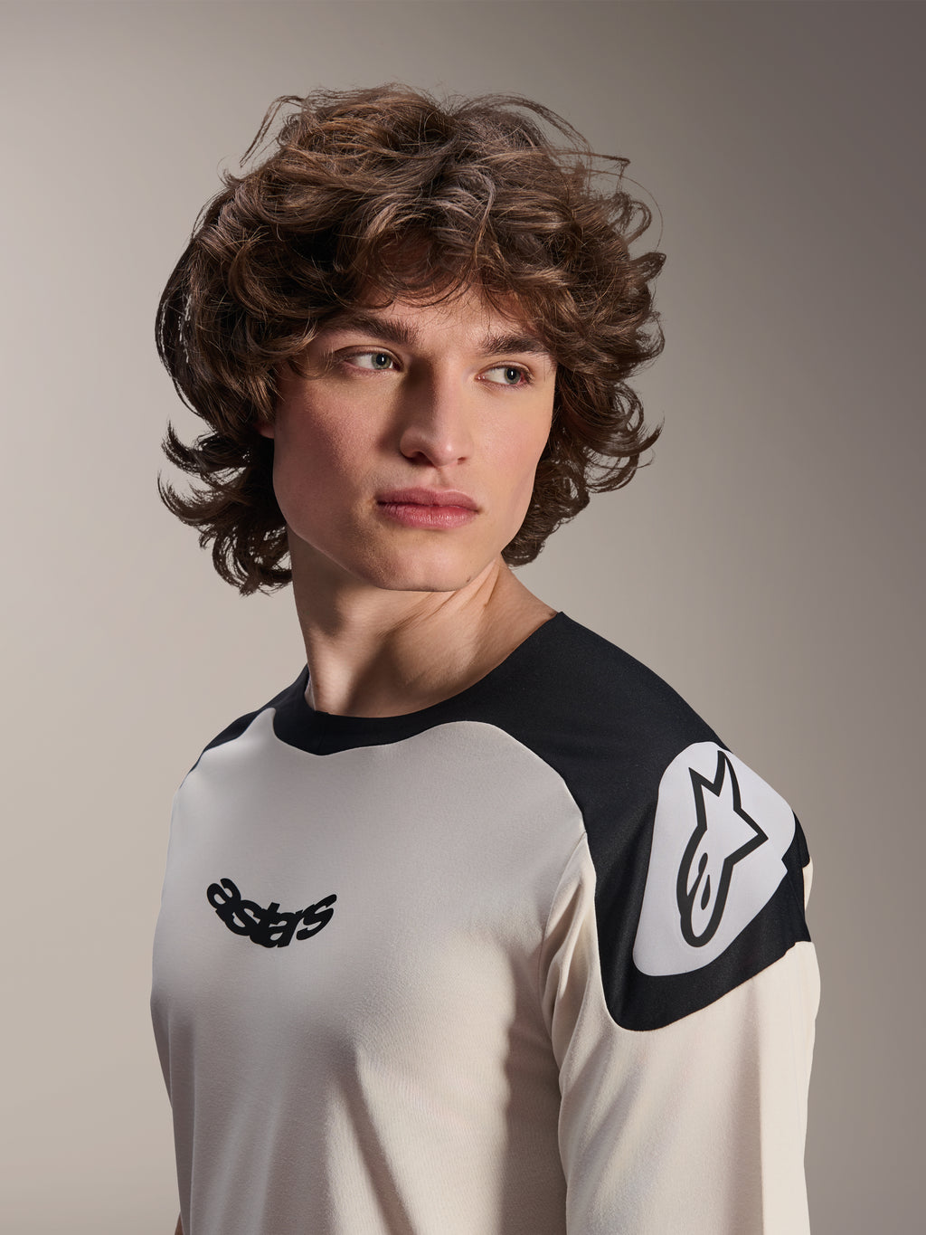 Camiseta de manga corta Alpinestars A-Aria Polartec Elite, color crudo con paneles negros en los hombros, con el logotipo astars negro en el pecho y el logotipo Astars blanco en el hombro, equipamiento de alto rendimiento para bicicleta de montaña usado por un modelo