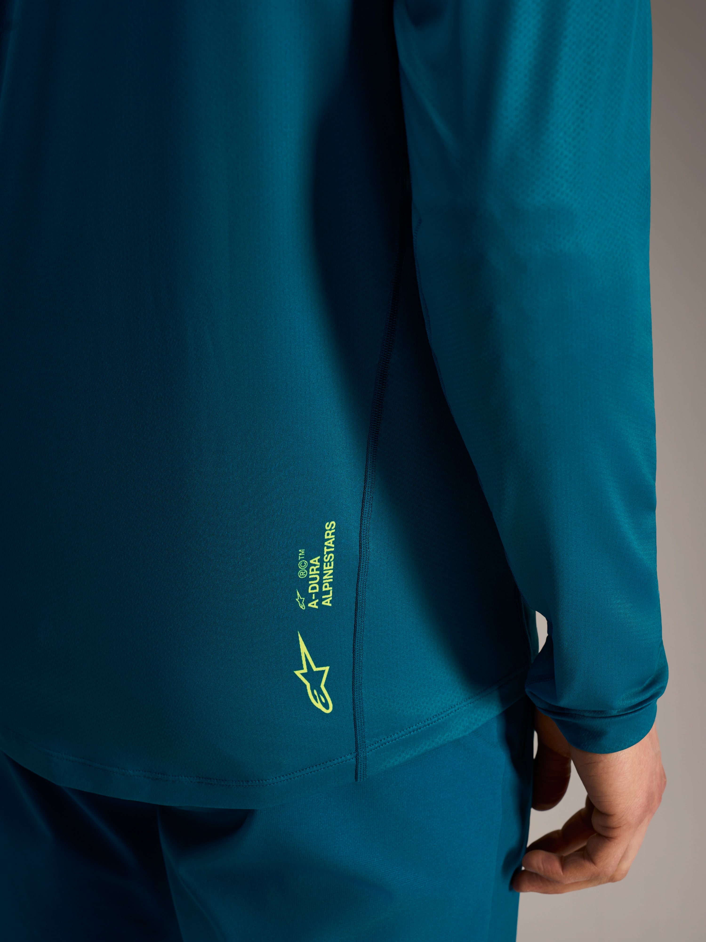 Jersey A-Dura Ride azul verdoso con logo Alpinestars verde lima en el dobladillo inferior trasero texturizado.
