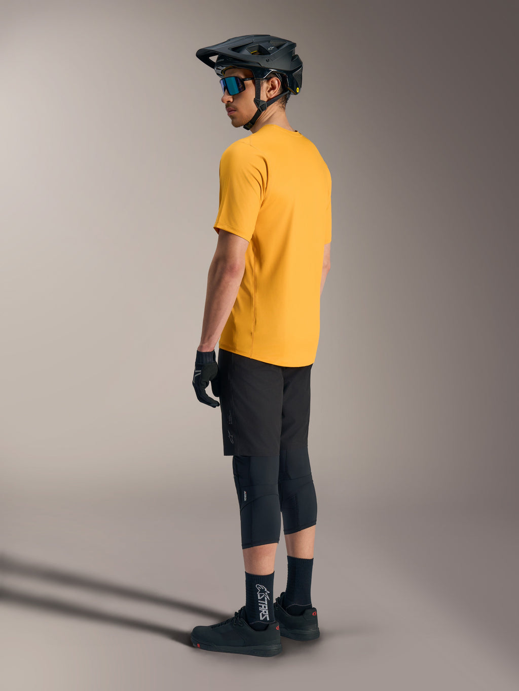 Jersey Alpinestars A-Dura Ride naranja de manga corta, vista trasera de ciclista con equipación de MTB negra y casco.