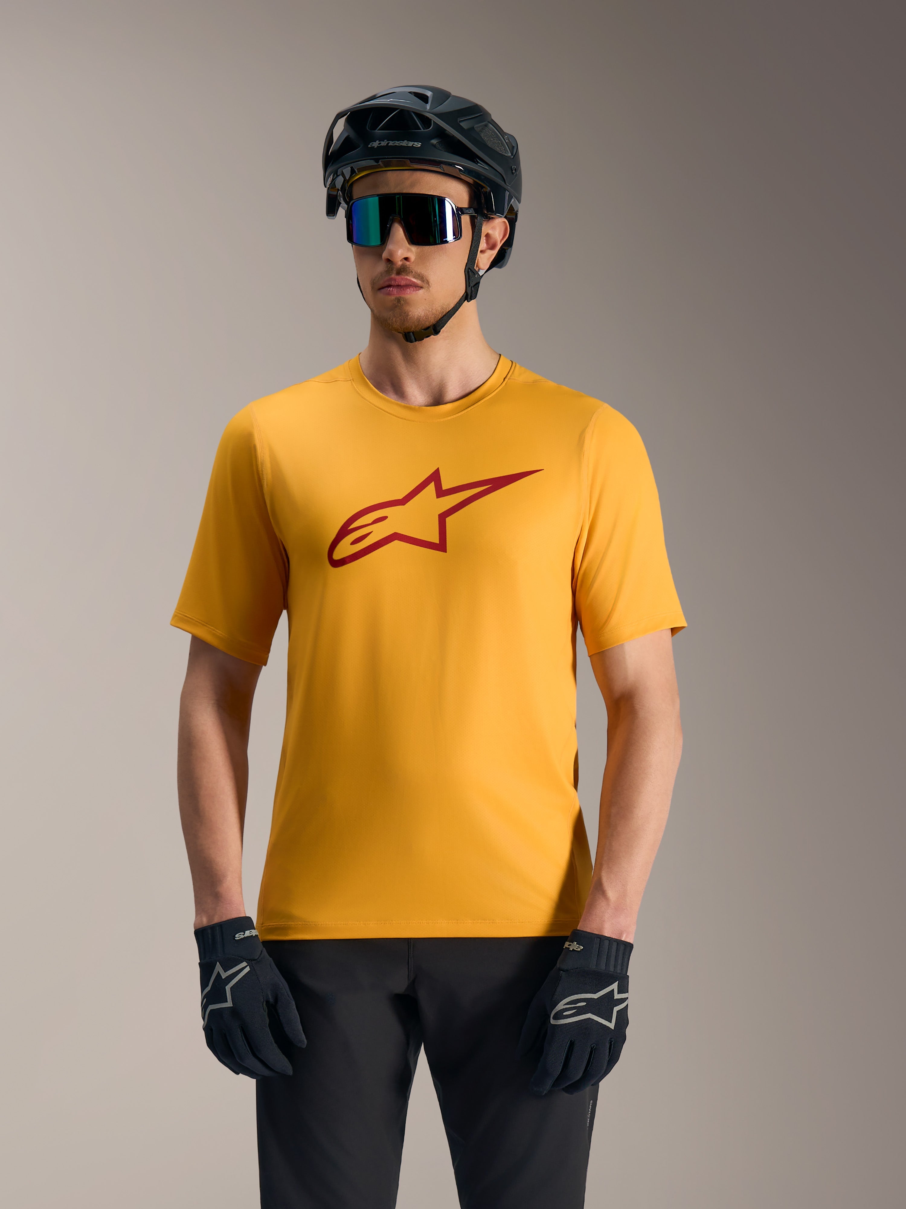 Camiseta A-Dura Ride naranja con logo Astars rojo, combinada con casco de ciclismo de montaña y guantes.