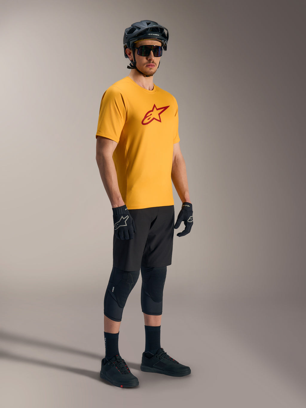 Camiseta Alpinestars A-Dura Ride naranja con logo rojo, equipo de montaña negro y casco de ciclismo.