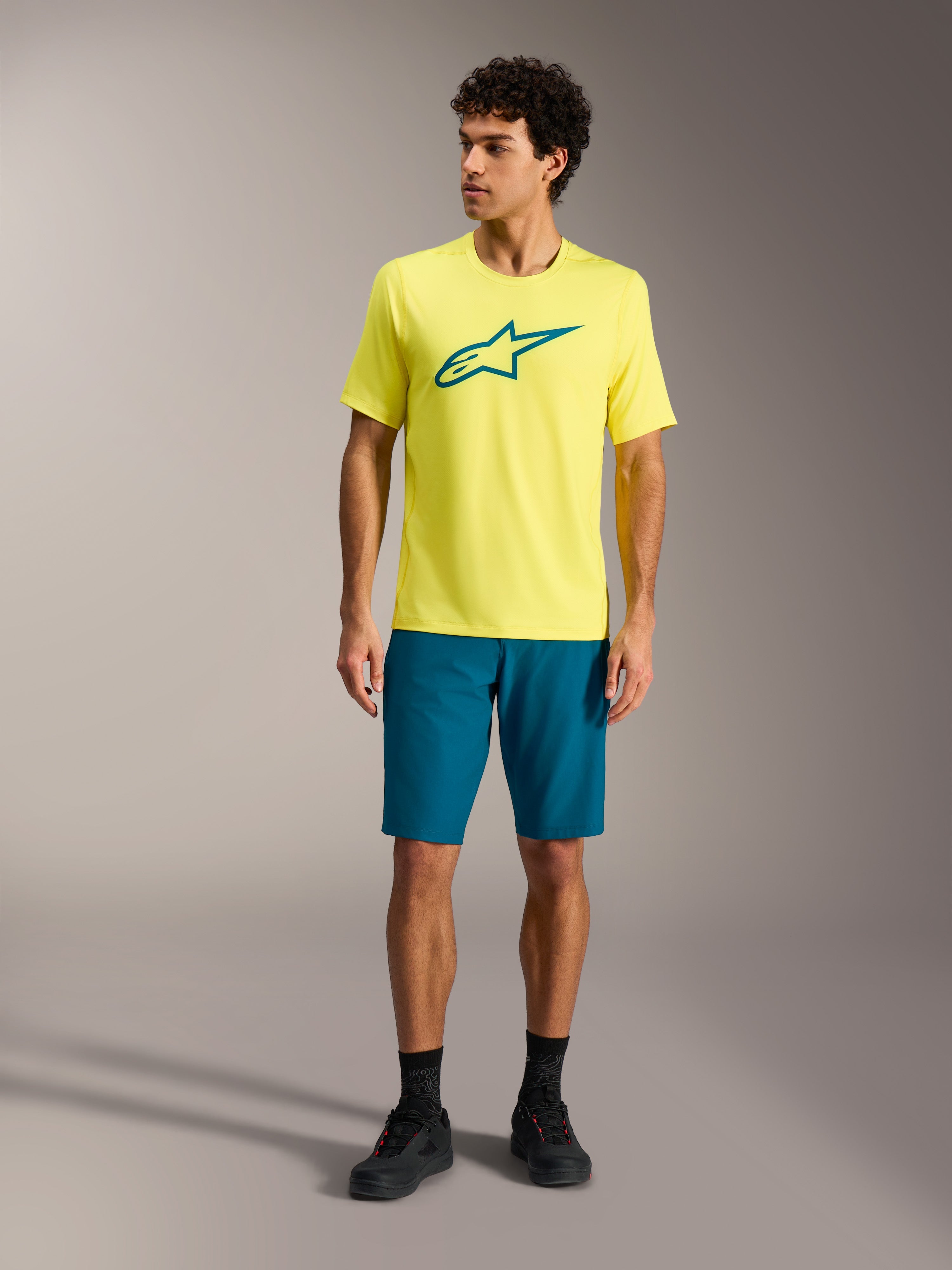 Jersey Alpinestars A-Dura Ride SS amarillo y pantalones cortos verde azulado, ropa técnica de MTB en estudio.