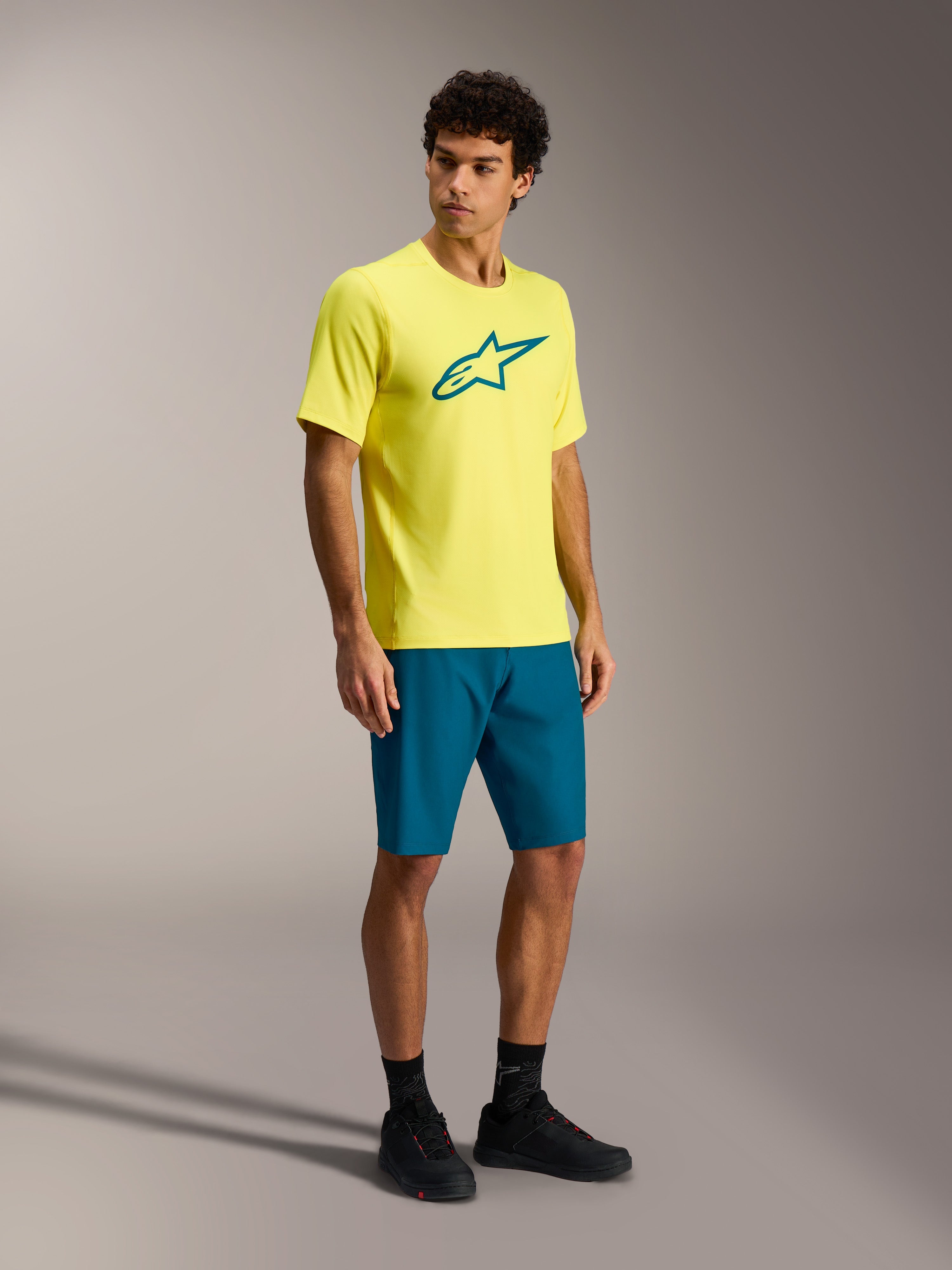 Conjunto MTB Alpinestars A-Dura Ride, jersey amarillo y pantalones cortos verde azulado sobre un modelo masculino.