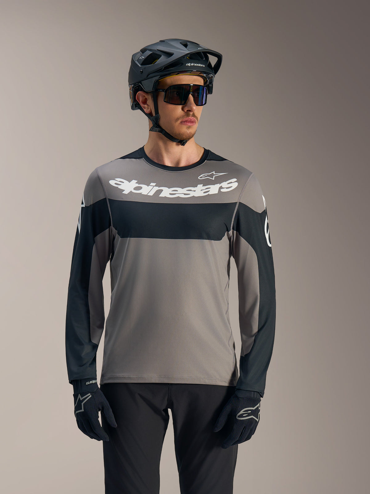 Camiseta de manga larga A-Dura Race gris y negra, logo Alpinestars blanco, combinada con casco de MTB para senderos.
