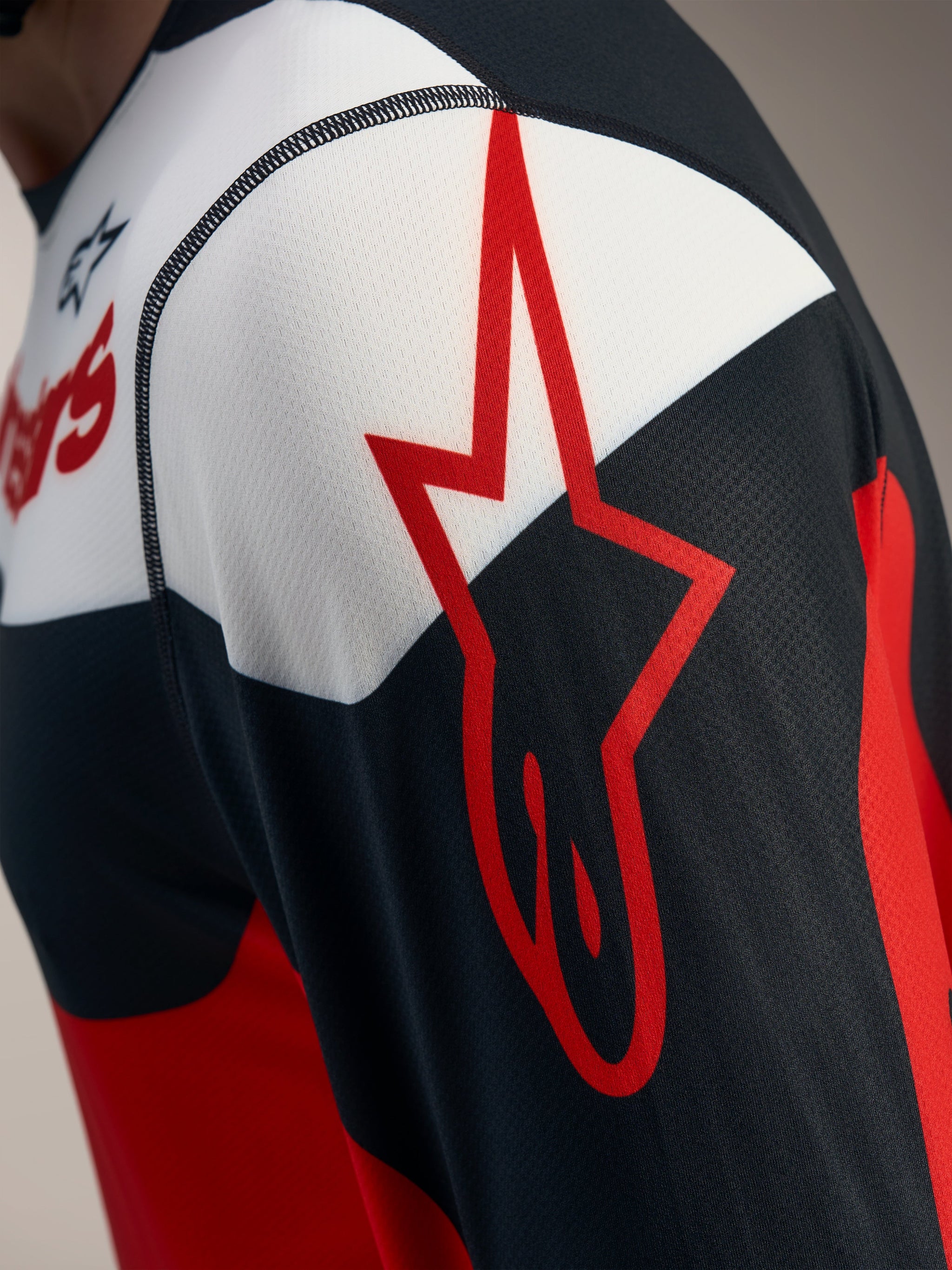Camiseta A-Dura Race Alpinestars roja y negra, detalle del logo de estrella sobre tejido de malla jacquard transpirable.