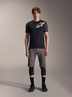 Jersey de manga corta Alpinestars A-Dura Lipan, negro con mangas gris jaspeado y logotipo Astars color canela en el pecho, usado por un modelo masculino con pantalones cortos de ciclismo de montaña grises y rodilleras negras, equipamiento técnico para MTB.