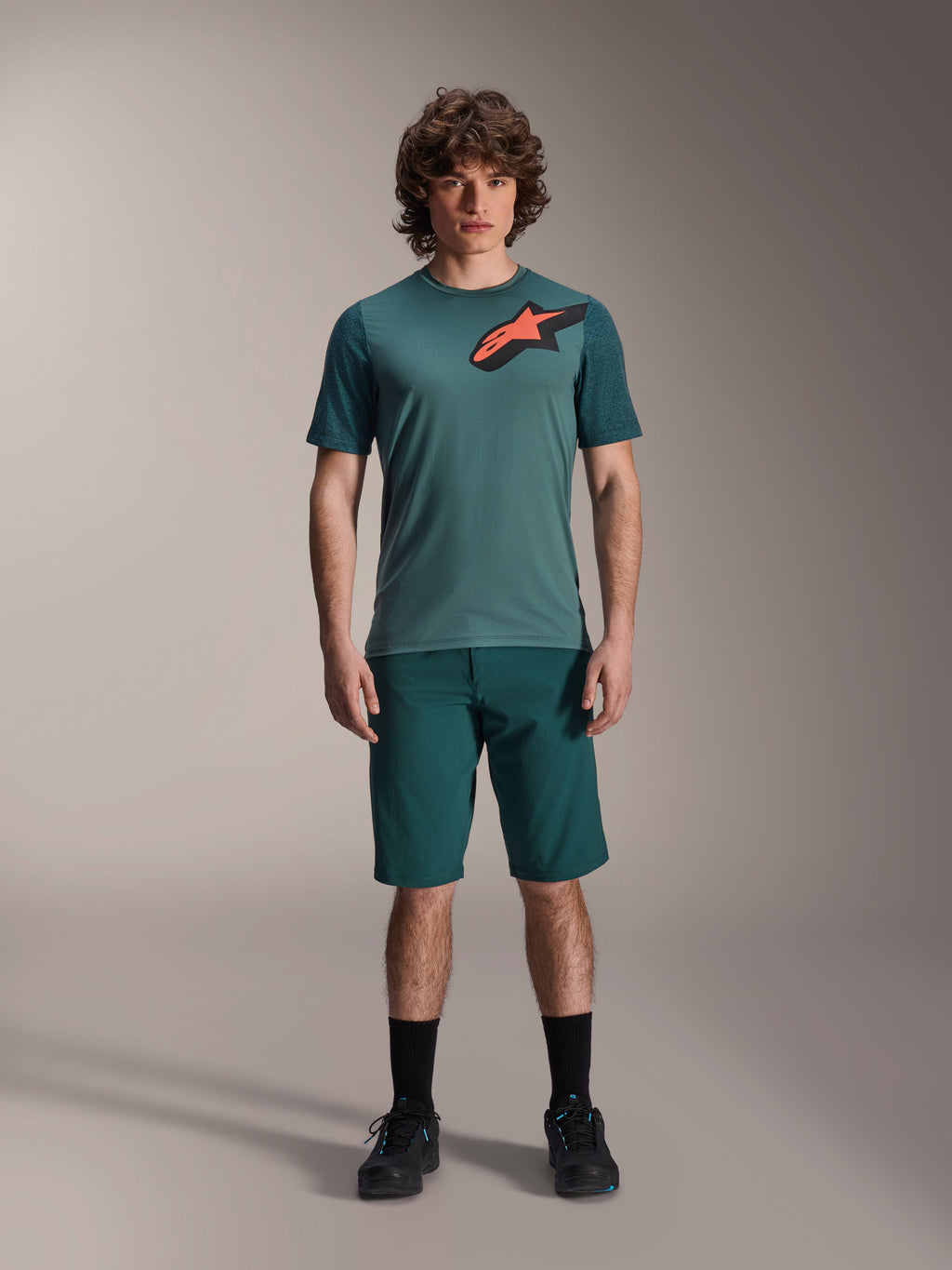Jersey Alpinestars A-Dura Lipan, jersey de MTB de manga corta, verde Silver Pine con logotipo Astars negro y naranja en el pecho, combinado con pantalones cortos a juego y calzado negro, ropa técnica para bicicleta de montaña