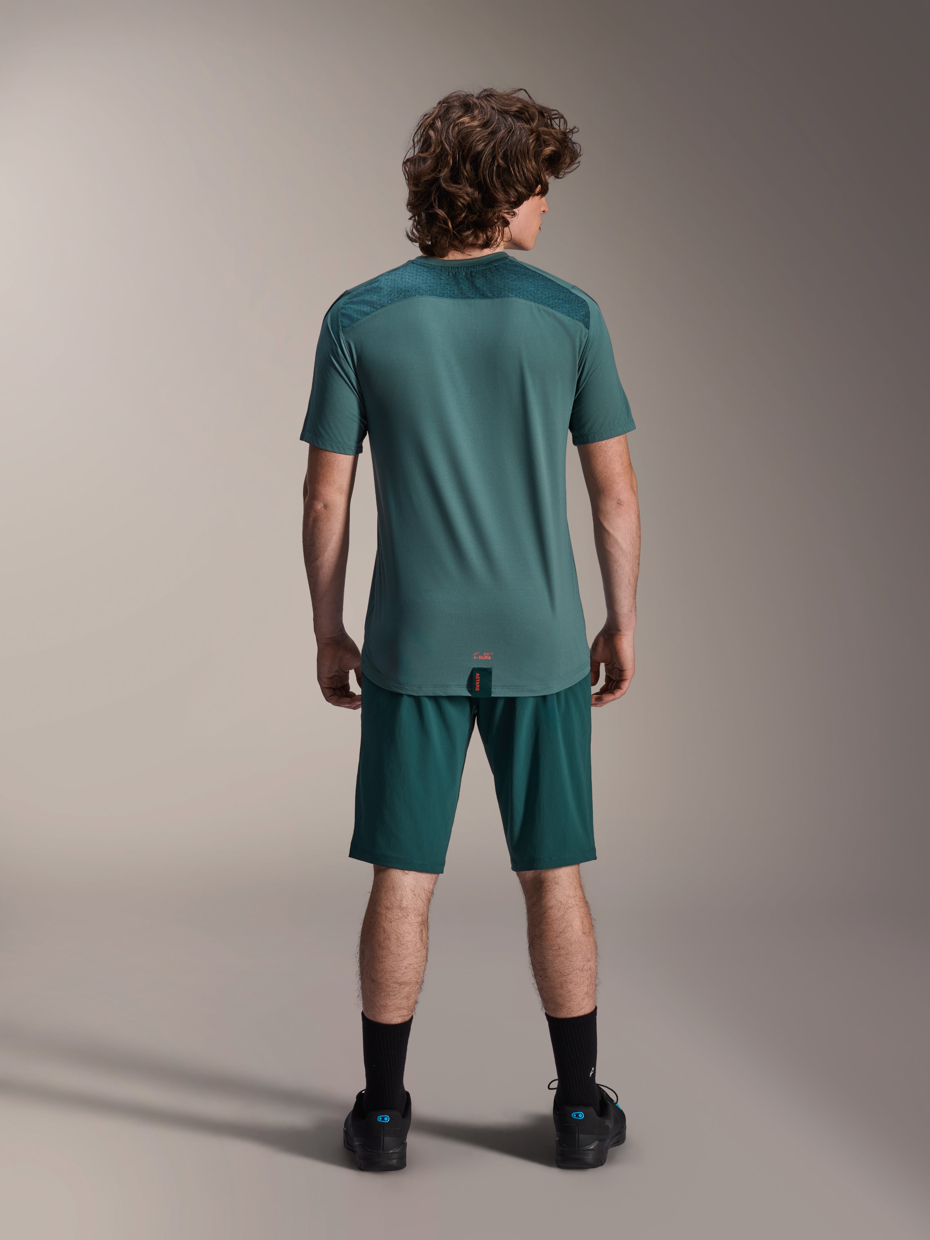 Alpinestars A-Dura Shorts y Jersey A-Dura Lipan SS, color verde Dark Pine, vista trasera en un modelo, ropa de alto rendimiento para bicicleta de montaña que incluye jersey de manga corta y shorts a juego, equipación de ciclismo off-road