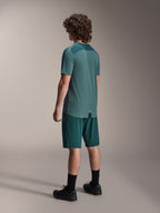 Modelo con shorts Alpinestars A-Dura en color Dark Pine y jersey de manga corta Lipan verde a juego, vista posterior, combinados con calcetines negros y zapatillas de ciclismo de montaña negras, equipamiento profesional de MTB