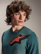Alpinestars A-Dura Lipan Jersey, camiseta de MTB de manga corta, Silver Pine, presenta un prominente logotipo de Astars en rojo y negro en el pecho, mangas de jacquard texturizadas, retrato en primer plano de un modelo con equipamiento de ciclismo de alto rendimiento
