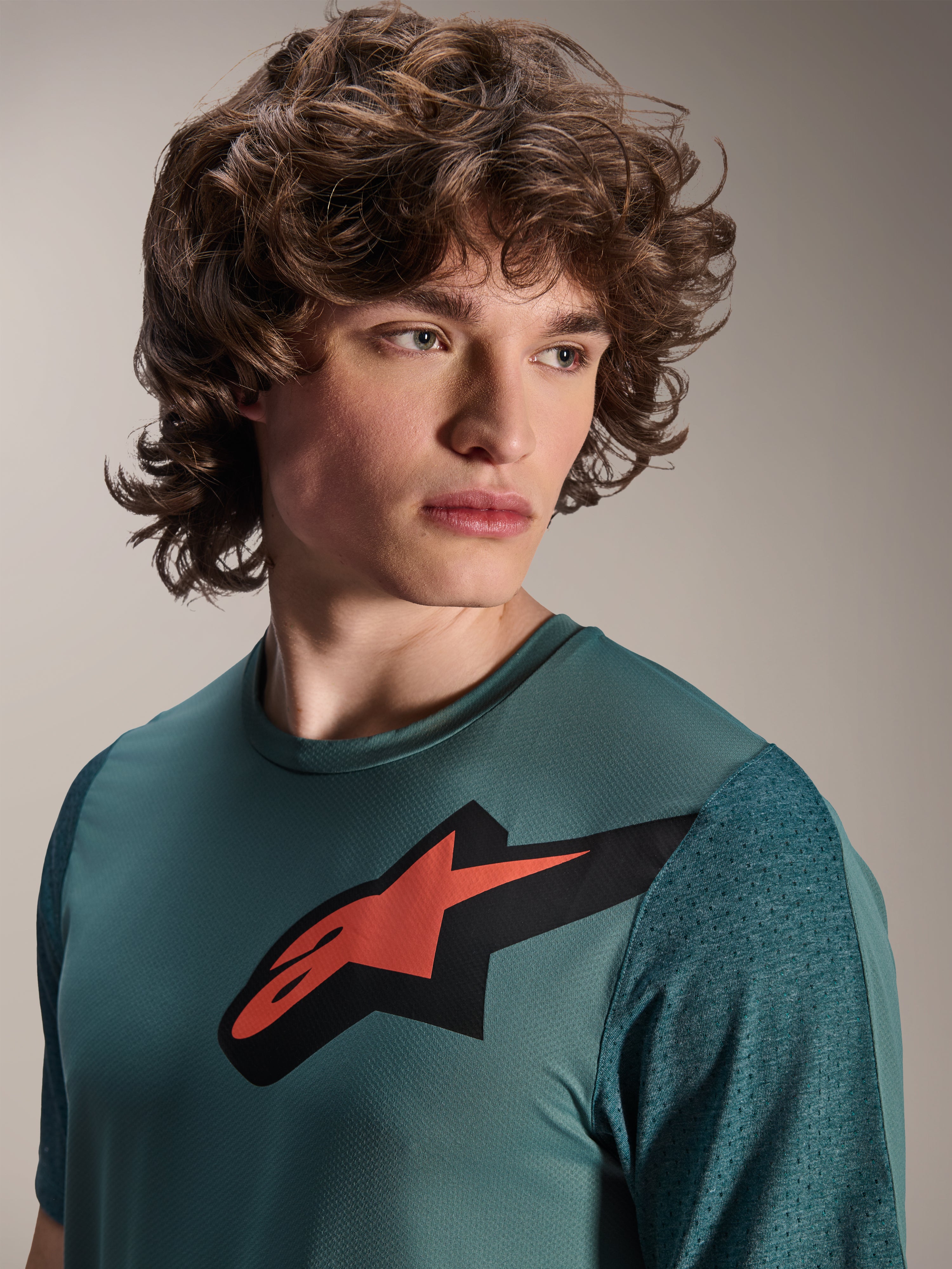 Alpinestars A-Dura Lipan Jersey, camiseta de MTB de manga corta, Silver Pine, presenta un prominente logotipo de Astars en rojo y negro en el pecho, mangas de jacquard texturizadas, retrato en primer plano de un modelo con equipamiento de ciclismo de alto rendimiento
