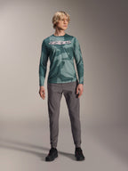 Jersey de manga larga Alpinestars A-Dura Hollow Camo, color Silver Pine Camo con patrón de camuflaje verde, logotipo "astars" grande en blanco en el pecho, combinado con pantalones técnicos grises y zapatillas de ciclismo negras, equipamiento de MTB de alto rendimiento