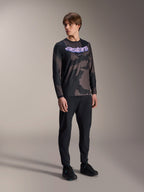 Modelo masculino con el jersey de manga larga Alpinestars A-Dura Hollow Camo, estampado Black Camo con gráfico morado 'astars' en el pecho, combinado con pantalones técnicos negros y zapatillas negras, equipamiento casual de MTB
