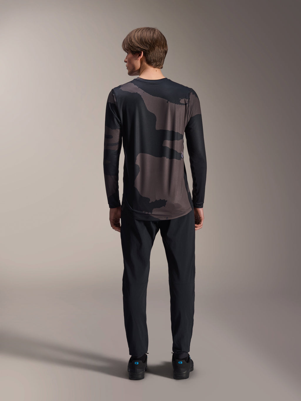 Alpinestars A-Dura Hollow Camo Jersey de manga larga, Black Camo, vista trasera con pantalones negros, con un patrón de camuflaje oscuro y dobladillo trasero más largo para cobertura de MTB.